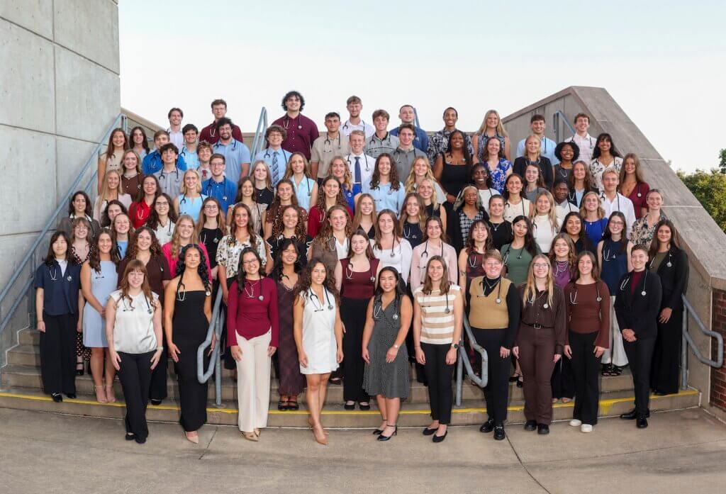 A very large group is gathered on steps for an outdoor-set photo. All of the people are wearing stethoscopes and are dressed in business casual attire