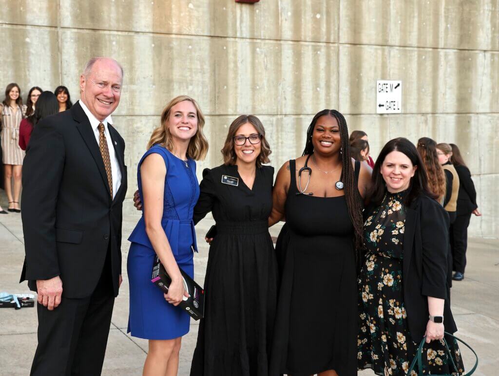 six people are standing together outside in front of a concrete wall