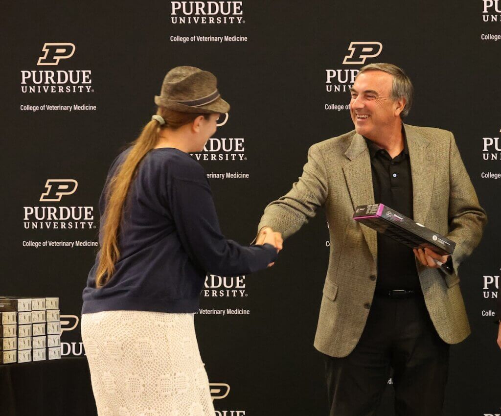two people are shaking hands in front of a Purdue University backdrop.