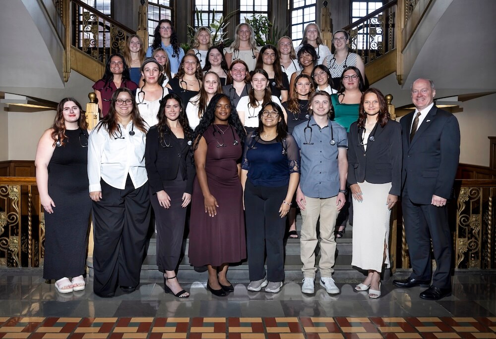 A large group is gathered on a set of indoor stairs for a group photo, all wearing business professional attire.