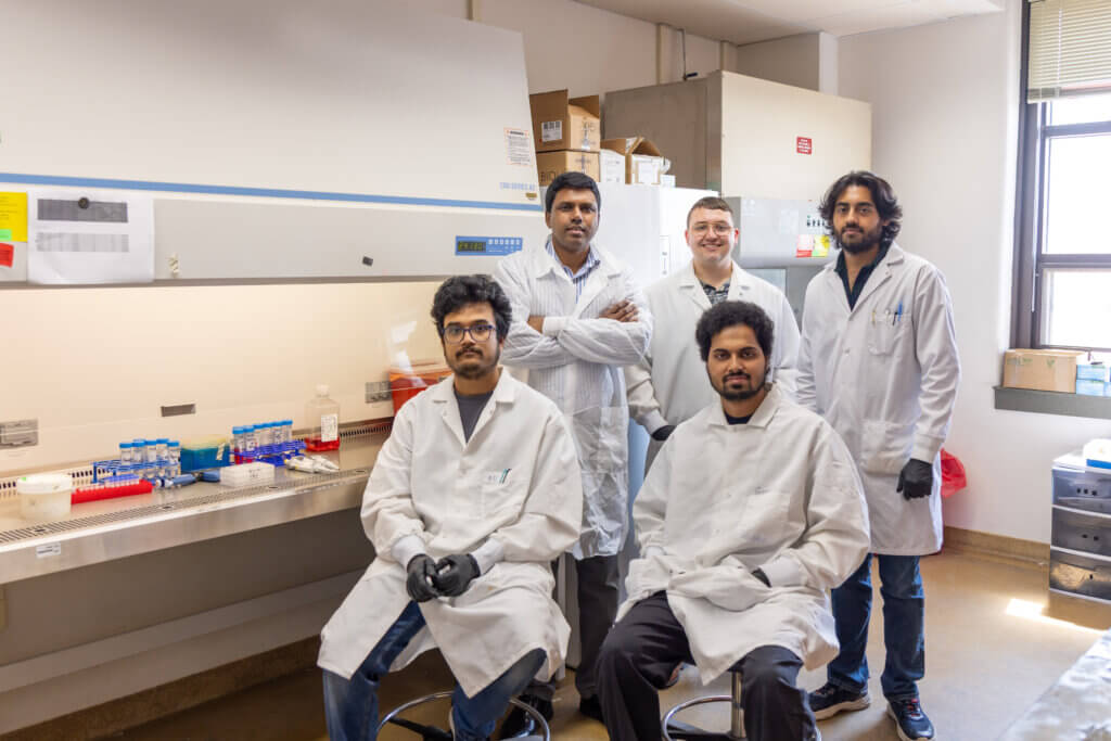 group of 5 people wearing white lab coats in a laboratory setting