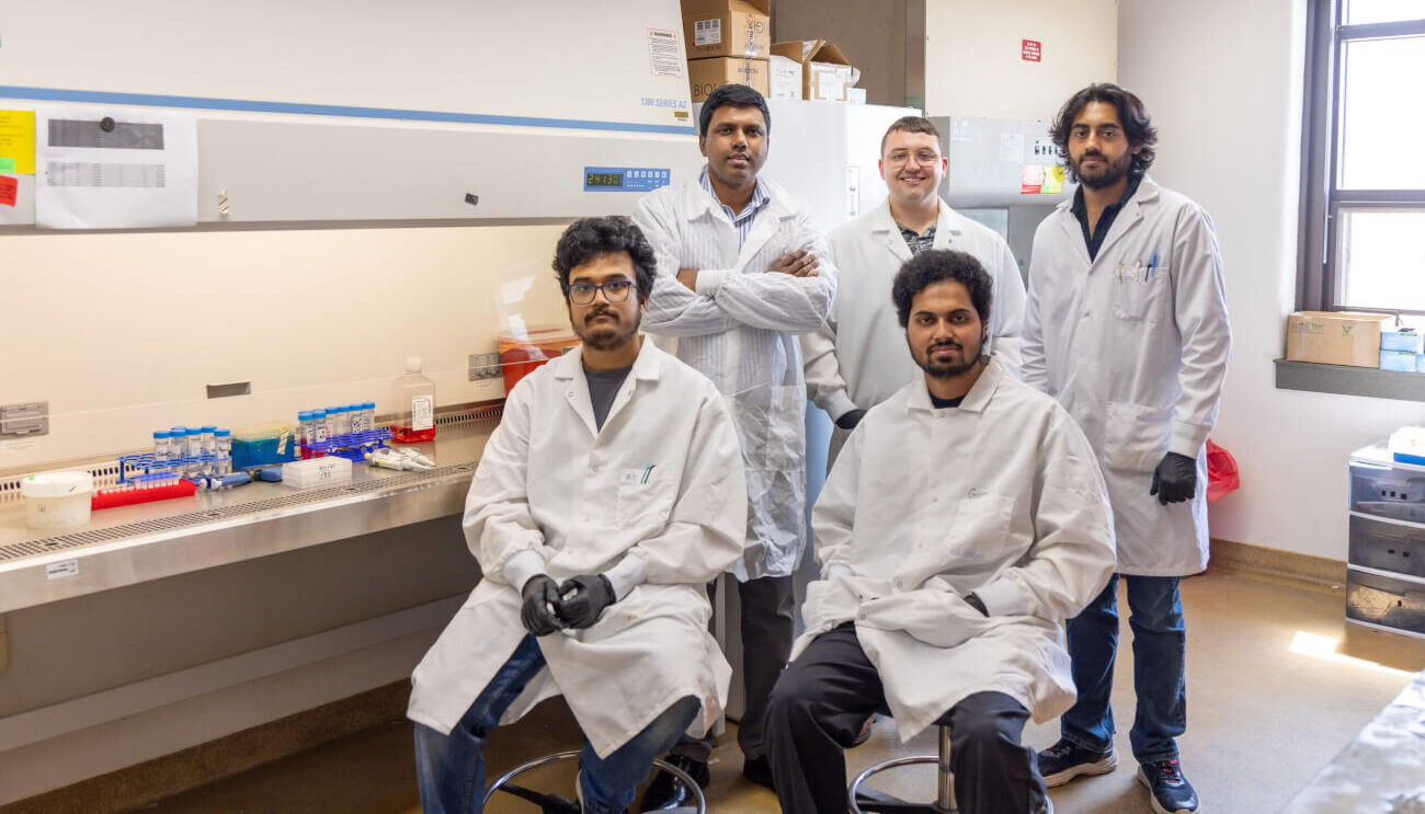 group of 5 people wearing white lab coats in a laboratory setting