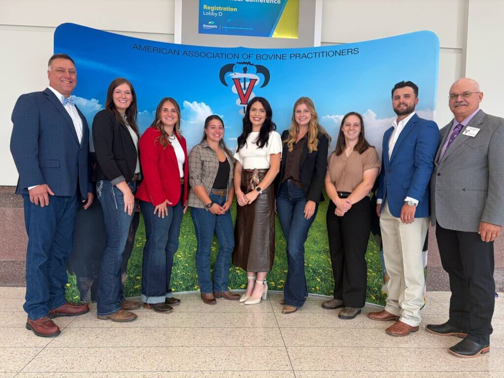 A group of nine individuals stands in front of a natural-looking backdrop that reads "AMERICAN ASSOCIATION OF BOVINE PRACTITIONERS"