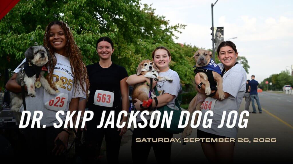 four people are standing outdoors in running attire. Three of the four people are holding small dogs.