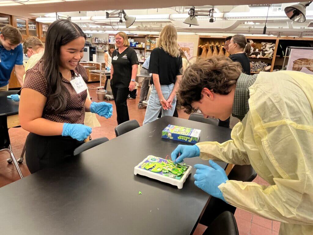 two people are featured in the photo, wearing personal protective equipment in a laboratory classroom setting