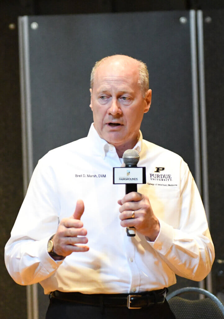 A man wearing a long sleeve white shirt is speaking into a microphone
