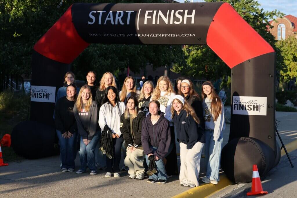 A large group of people are standing under the start/finish line at an outdoor race event