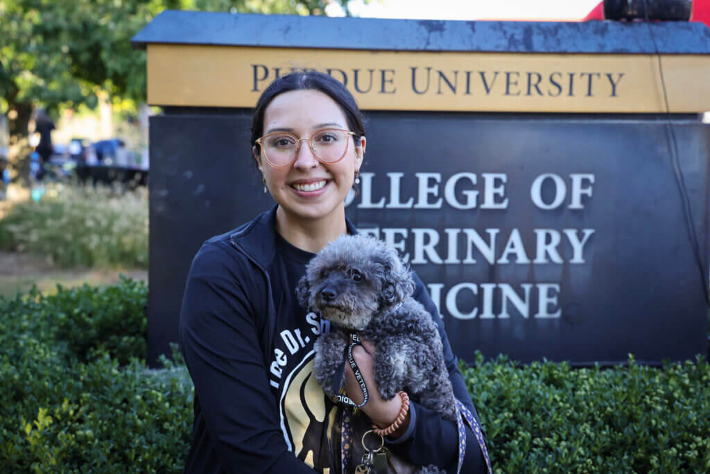 A person is embracing their dog in front of a sign that reads "Purdue University College of Veterinary Medicine"