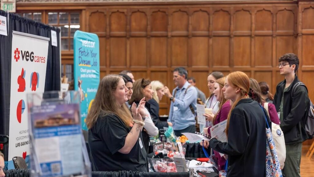 A group of people appear to be attending a convention of various vendors and booths, and are in conversation with one another