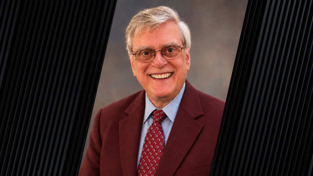 portrait of a person with gray hair, glasses, and wearing a red suit jacket and tie
