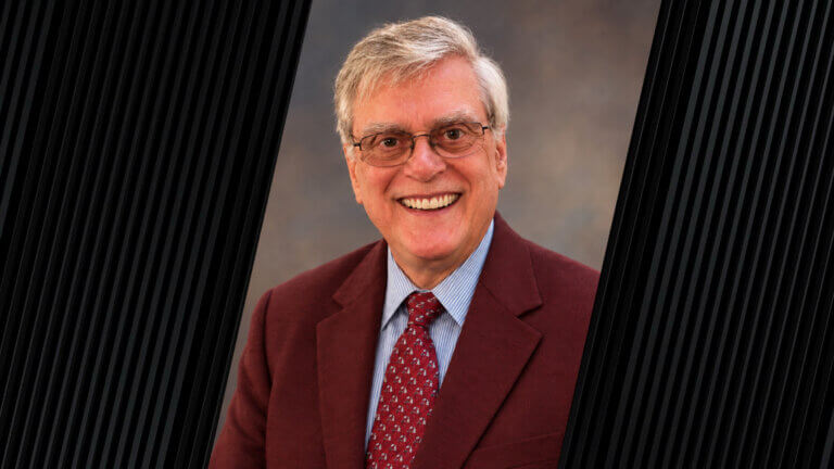 portrait of a person with gray hair, glasses, and wearing a red suit jacket and tie