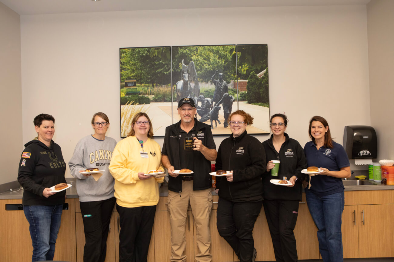 A group of seven people are standing at a countertop. They are all holding cups and plates of food.