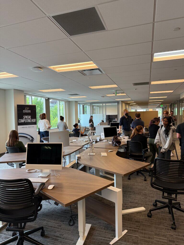 A large room is pictured with computer screens and people appearing to be moving and in conversation with one another.