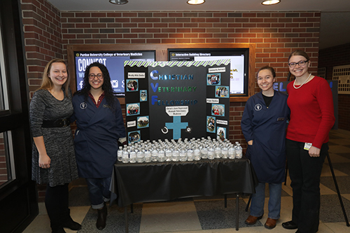 Members of the Christian Veterinary Fellowship student organization host a display table with water for visiting families (left-right): Hannah Clinton, CVF president; Jessica Linder, treasurer; Katelyn Gnegy and Emily Christenson, social and mission chair.